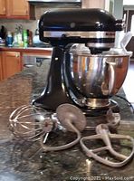 Black tilt-head stand mixer with stainless steel bowl and accessories on countertop
