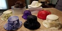Photo of eight fashion hats arranged on a bed showing a variety of colors and styles including spring/summer and fall/winter hats.