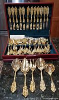 Full display of gold plated FB Rogers flatware set with ornate floral and scroll handle detailing in wooden case.