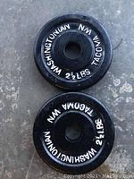 Topview of two black round weight plates with white 'Washingtonian NW Tacoma' and '2 1/2 LBS' markings, showing condition and lettering