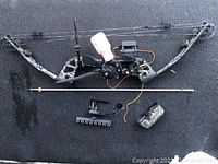 Full view of camo compound bow with attached fishing line spooler, arrow rest, included arrow, line spool mount, and small fabric accessory.