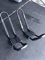 Side view of two kayak roof rack mounts showing padded support bars and securing plates with bolts.