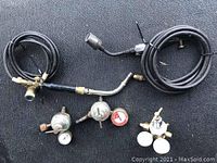 Miscellaneous used welding gas regulators, pressure gauges, and hoses with torch handles laid on a black surface.