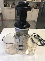 Full view of the Omega VRT350 juicer with two clear plastic containers in front, showing the vertical black and silver design with power cord.