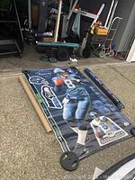 Full view of Matt Hasselbeck Seahawks Fathead decal unrolled on driveway with original rolled packaging tubes next to it and black weights on corners.