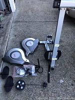 Disassembled rowing machine parts, showing large silver plastic casing units, metal frame parts, foot pedals, and monitor cable.