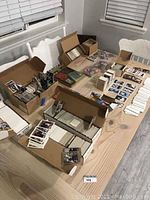 Wide view of table with several boxes full of trading cards, including some loose cards spread out. Shows quantity and packaging style of lot.