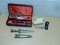 Full lot overview showing boxed steak knife set, Buck folding knife with sheath and box, and decorative dagger with sheath.