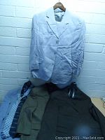 Front view of light blue suit jacket with other suits and ties beneath it, showing clothing items and condition.