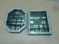 Two black wooden shadowboxes placed side by side on a flat surface, showing glass fronts and compartments.