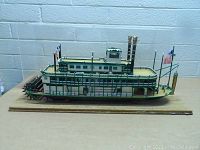 Full side view of the large paddlewheel riverboat model showcasing the detailed green railings, smokestacks, and flags inside the wooden case.