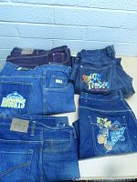 Five pairs of jeans shown from back with distinctive embroidered and branded back pockets including Nuggets, Mega, Songs of Freedom, and floral design.