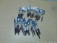 Overview photo of entire vintage flatware set arranged on a table, showing forks, knives, and spoons with brown handles and decorative metal necks.