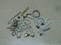 Overview of miscellaneous jewelry including pearl necklaces, metal chains, rings, bracelet, clip-on earrings, and other small jewelry parts on a white surface.