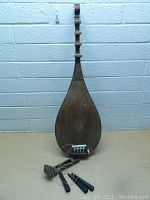 Full front view of wooden stringed instrument with teardrop body, strings, bridge and accessories included on table in front.