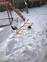 Full view of the yellow metal child's digger toy with black seat and hand controls shown in snow.