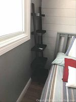 Side view of one black ladder shelving unit placed adjacent to bed and wall, showing shelves and height