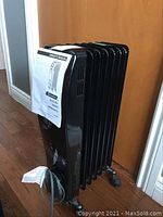 Front angle view showing the attached owner's manual and caster wheels on a six-finned black electric oil-filled radiator heater.