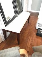 Full view side angle of bench showing rectangular ultra suede cushioned top and dark wooden legs on hardwood floor.