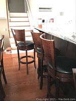 Three dark wood bar stools with black round upholstered seats, curved wooden backrests, and circular footrest rings. The stools swivel and have some wear on backs.