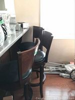 Photo showing 3 wooden bar stools in a row with black swivel seats and curved backs, positioned near counter.