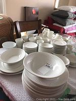 Wide view of white Johnson Bros fluted-edge dinnerware including multiple stacks of plates, bowls, cups and saucers on a table.