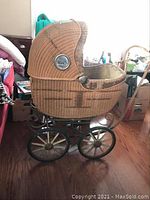 Side view of vintage wicker pram with curved canopy hood and visible port hole glass window on side, showing overall structure and wicker condition.