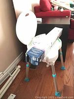 Side-angle view of the white plastic shower chair highlighting adjustable aluminum legs with blue rubber tips and the boxed grab bar placed on the seat.