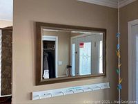 Wide shot of wall mirror mounted on a beige wall with a white coat rack below it and entrance door to the side.