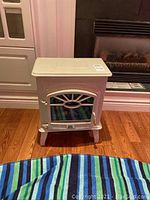 Front view of the white faux wood stove heater showing glass front and handle details.