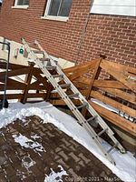 Full side view of the aluminum extension ladder leaned against a brick wall showing snow on the ground.
