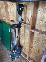 Side view of the Yardworks electric lawn edger standing upright in a wooden shed, showing the handle, motor housing, and wheels.