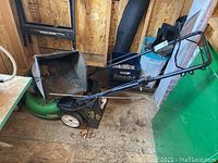 Full side view of the green LawnBoy push mower with black handle, placed on a wooden floor inside a shed.