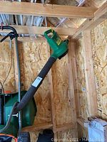 Photo showing the full length handheld leaf blower with green body and black tube against wooden wall background.