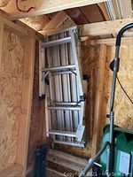 Photo showing the full aluminum painter's bench folded and positioned vertically against a wooden wall.