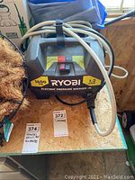 Full top view of Ryobi electric pressure washer on a surface with power switch and hoses coiled above.