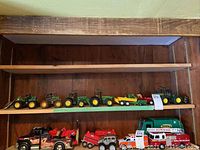 Two-shelf display showing multiple green John Deere tractors on top shelf and toy vehicles below