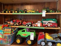 Full view of toy vehicles displayed on wooden shelves including tractors, tow trucks, ambulance, fire rescue truck, and a container of colorful building blocks.