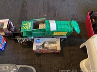 Display of both the Tonka recycling truck and boxed Car Quest diecast racing truck placed side by side on floor.