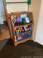 Overall view of the homemade dollhouse showing three levels with various miniature furniture and accessories inside a wooden cabinet structure.