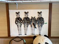 3D metal zebra wall hanging showing four zebras, black and white, standing in a row on a cream background framed by wooden border.