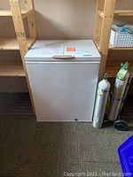 Full view of white Frigidaire commercial chest freezer between wooden shelves and oxygen cylinders.