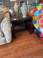 Pair of two dark brown square end tables with open shelf placed against living room furniture. Tables measure around 23x23x23 inches.