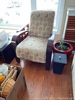 Full view of the accent chair showing patterned upholstery and wooden arms near window and plant.