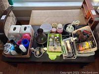 Wide view of all items arranged on a black table, showing tissue boxes, dispensers, diffuser, lamp, candles, and shoe shine basket.