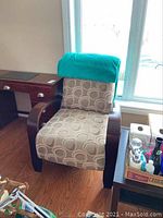 Front view of the beige accent chair with dark wooden arms and turquoise throw blanket on backrest.