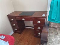 Full front view of the wooden desk showing all six drawers with metal cup pulls and black desk pad on top.
