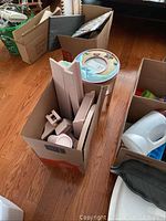 Several painted wooden pieces including shelves, panels, lamp, and furniture parts packed in a cardboard box