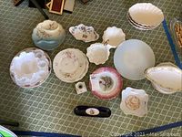 Full lot of assorted vintage plates, bowls and serving dishes arranged on the carpet, showing variety of shapes, colors, and markings.