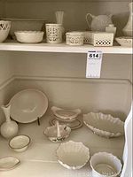 Photo showing white porcelain bowls, votive holders, small dishes, and a pitcher on shelf.